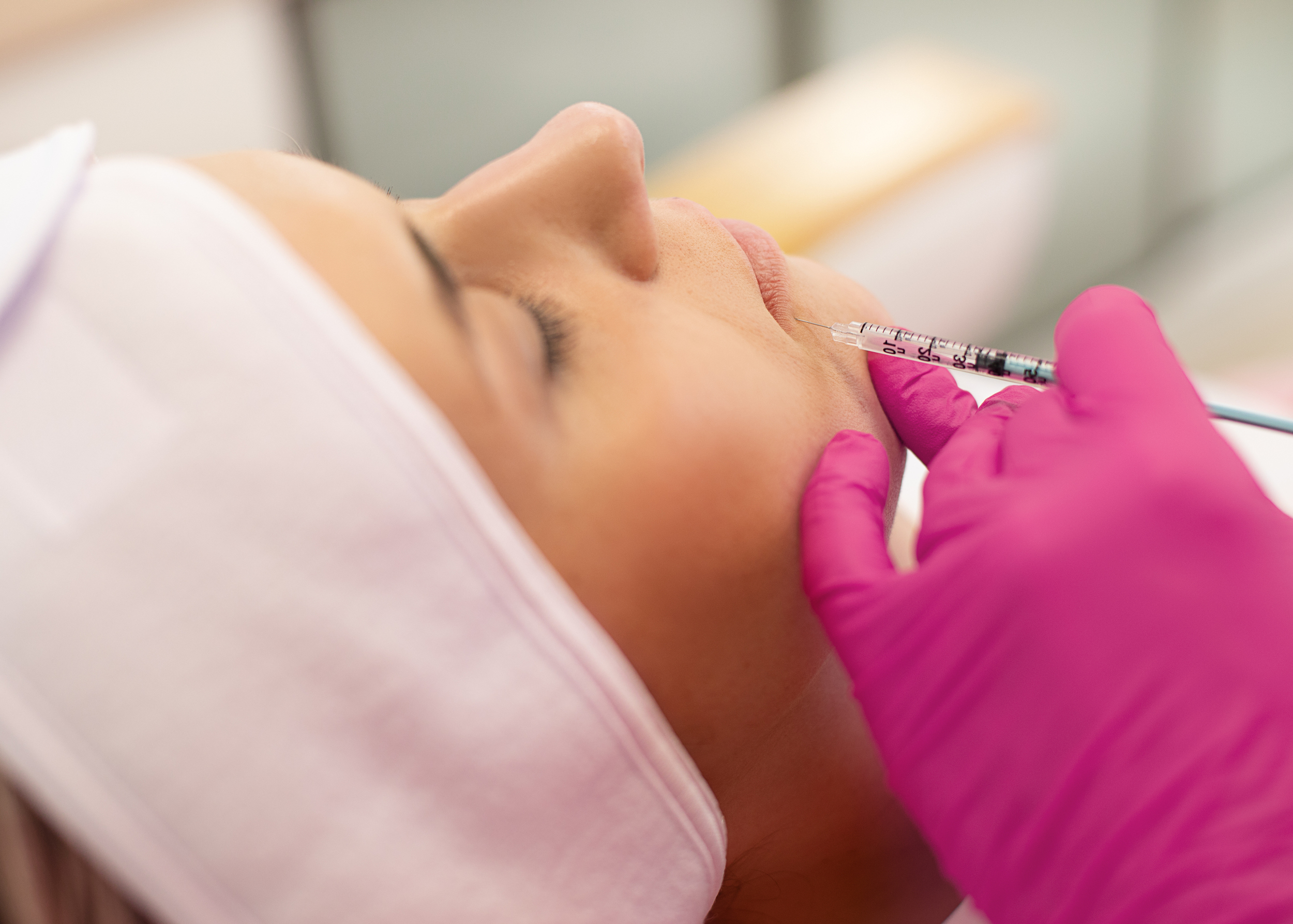 Side view of young woman getting rejuvenation beauty collagen injection into lips activating cells. Cosmetologist making anti-wrinkle procedure in pink gloves in beauty salon. Cosmetology, skincare.